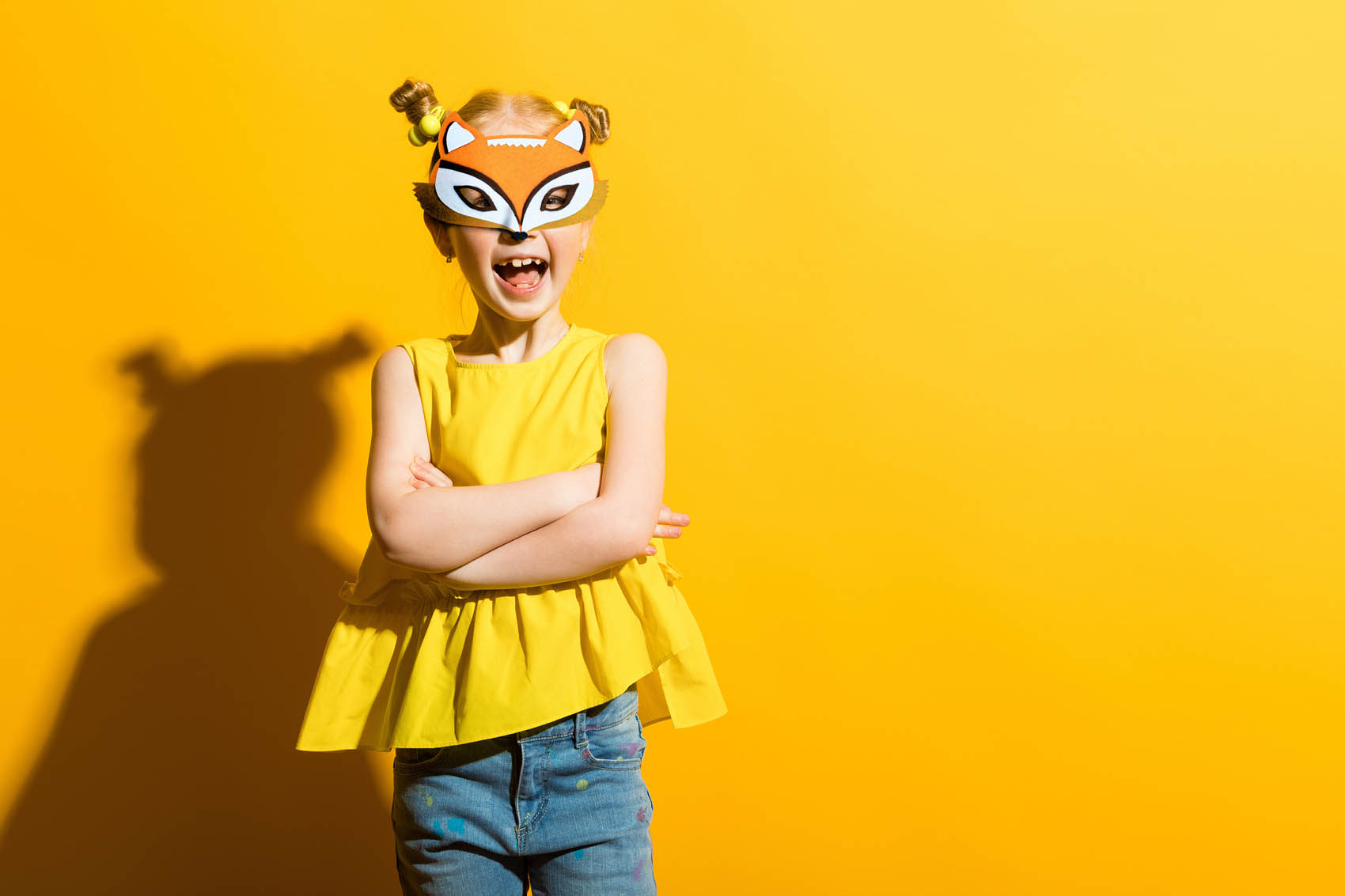 Petite fille avec couettes souriant, avec un masque renard sur le visage, sur fond jaune