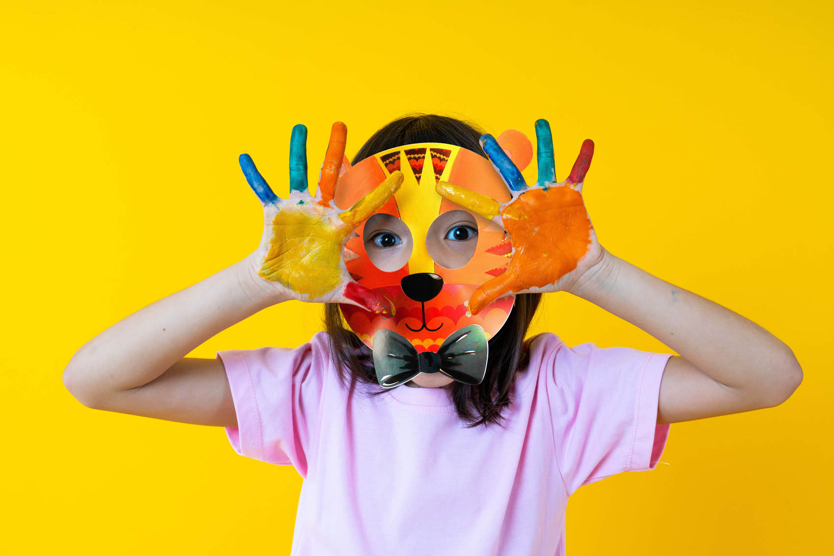 Enfant avec masque lion colorié qui écarte des mains pleines de peinture