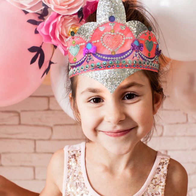 Petite fille en habit de fête souriant avec couronne décorée sur la tête et ballons derrière