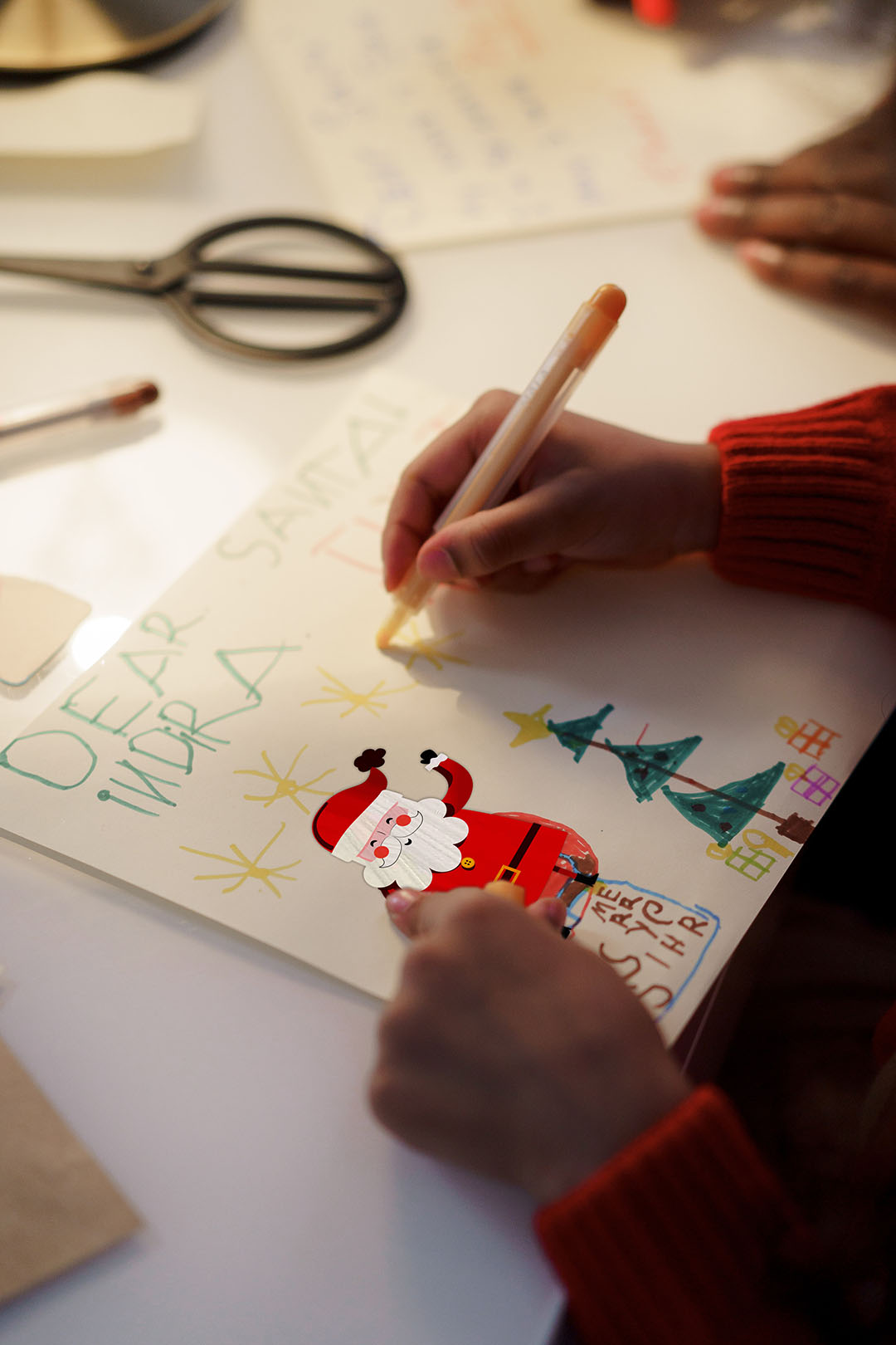 Mains d'enfant dessinant un sapin de Noël avec gommette Père Noël.